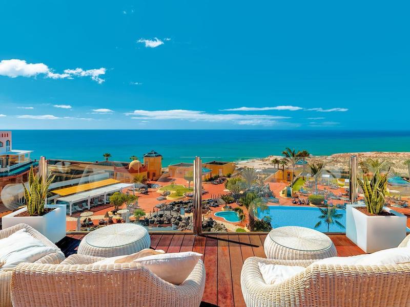 Area salotto esterna di lusso con vista su un resort tropicale e l'oceano sotto il cielo blu