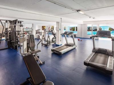 Moderne Fitnessraum mit Laufbändern, Kraftmaschinen und blauem Boden in hellem Raum.