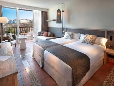 Helles Hotelzimmer mit zwei Doppelbetten, Balkon, modernen Lampen und Fliesenboden.