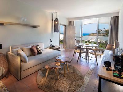 Moderner Wohnraum mit Sofa, Holztisch, Korb, Teppich und großem Fenster mit Meerblick.