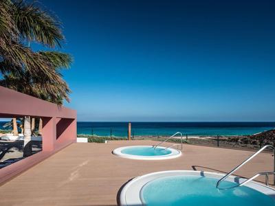 Poolbereich mit rundem Whirlpool, braunem Boden und Blick auf das blaue Meer und klare Himmel.