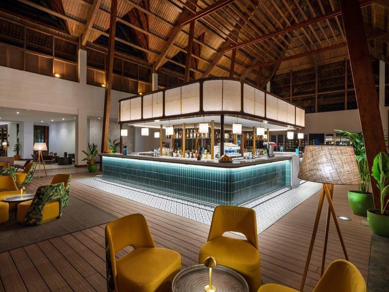 Moderní hotelová restaurace s otevřenými prostory, žlutými židlemi a dřevěnou střešní konstrukcí.