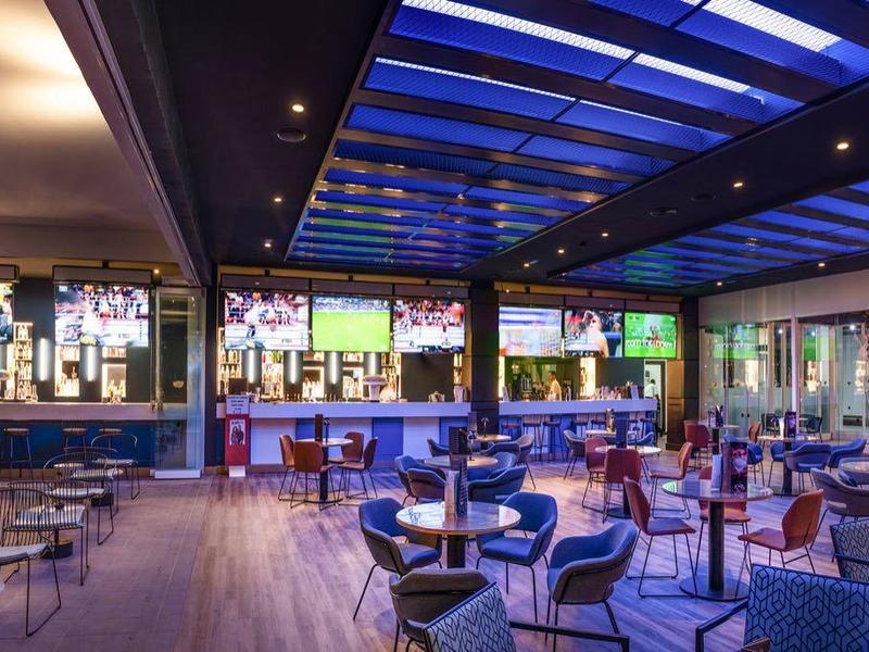 Moderní otevřená hotelová vnitřní sezení s modře osvětlenou skleněnou střechou a židlemi