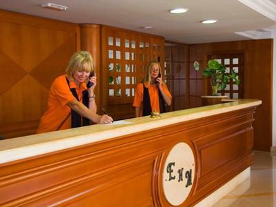 Réception avec deux employées en uniformes orange derrière un comptoir en bois.