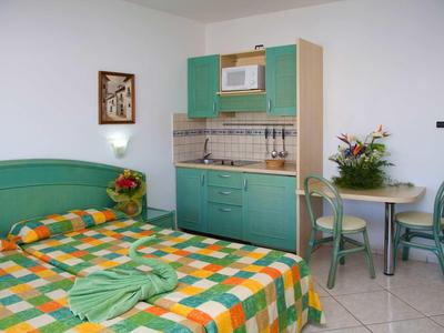 Petite chambre avec kitchenette, mobilier vert et une table avec deux chaises.