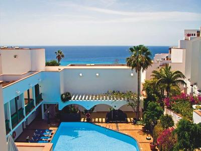 Hôtel avec piscine et chaises longues, entouré de palmiers, avec vue sur la mer sous un ciel bleu.