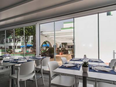 Nowoczesna restauracja z białymi krzesłami i niebiesko nakrytymi stołami przy dużych oknach.