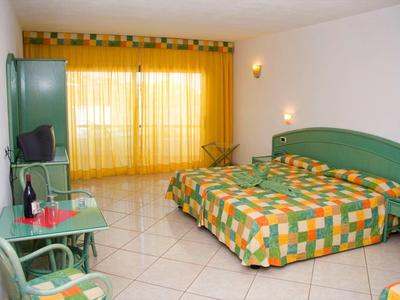 Chambre d'hôtel avec lit double, literie à carreaux verts et orange, et rideau jaune