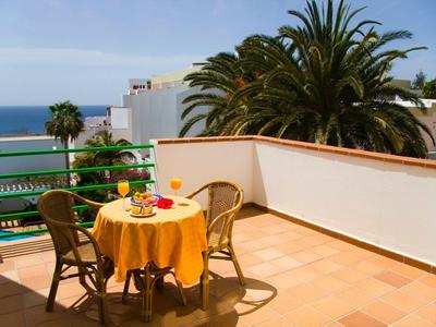 Terrasse avec table et chaises, vue sur des palmiers et la mer en arrière-plan.