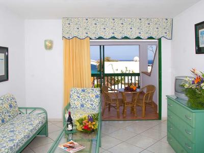 Salon lumineux avec meubles à motif floral et terrasse avec vue sur la mer.