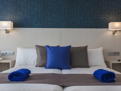 Chambre d'hôtel moderne avec lit double, coussins bleus et éclairage cosy.