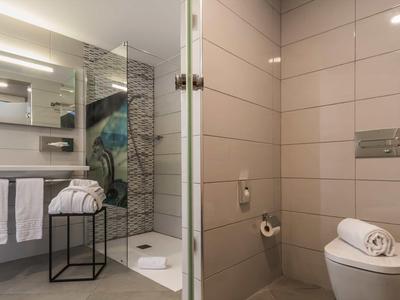 Salle de bain moderne avec douche à l'italienne, toilettes et serviettes dans un design lumineux.