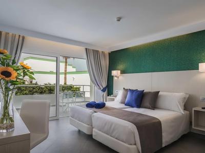 Chambre d'hôtel moderne avec lit double, mur d'accent vert et balcon avec vue sur l'eau.