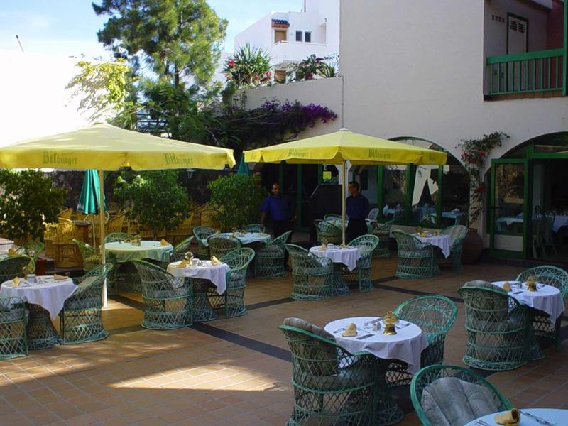 Espace extérieur avec tables, chaises et parasols jaunes à côté d'un bâtiment blanc.
