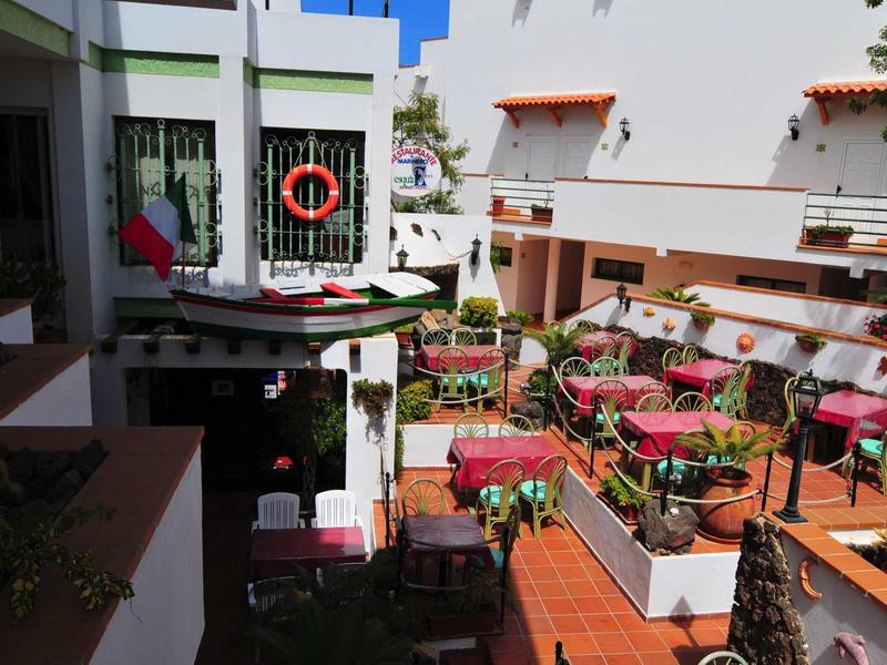 Cour intérieure d'un hôtel avec des sièges extérieurs, tables couvertes de nappes rouges et parasols.