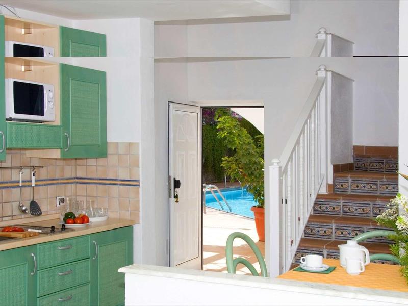 Petite cuisine avec armoires vertes à côté d'une porte ouverte menant à la piscine et un escalier en arrière-plan.