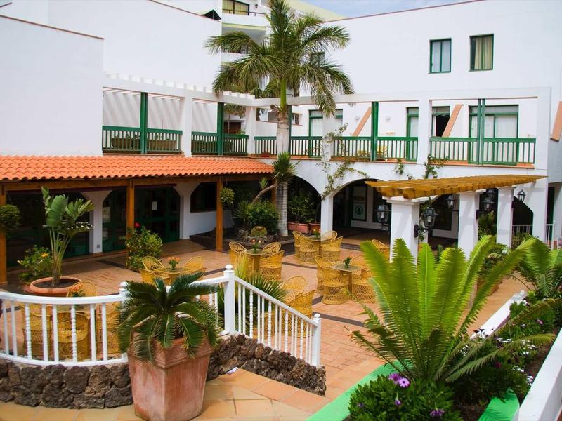 Cour intérieure d'hôtel avec bâtiments blancs, plantes tropicales et espaces assis.