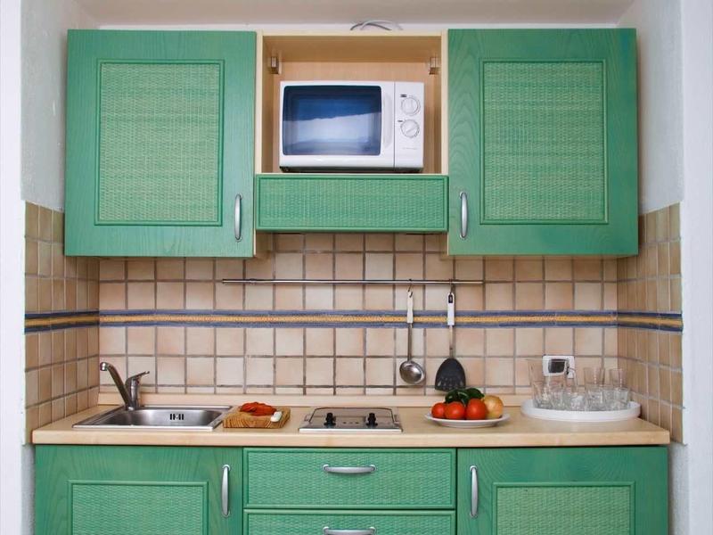 Petite cuisine avec armoires vertes, micro-ondes, évier et plan de travail avec nourriture.