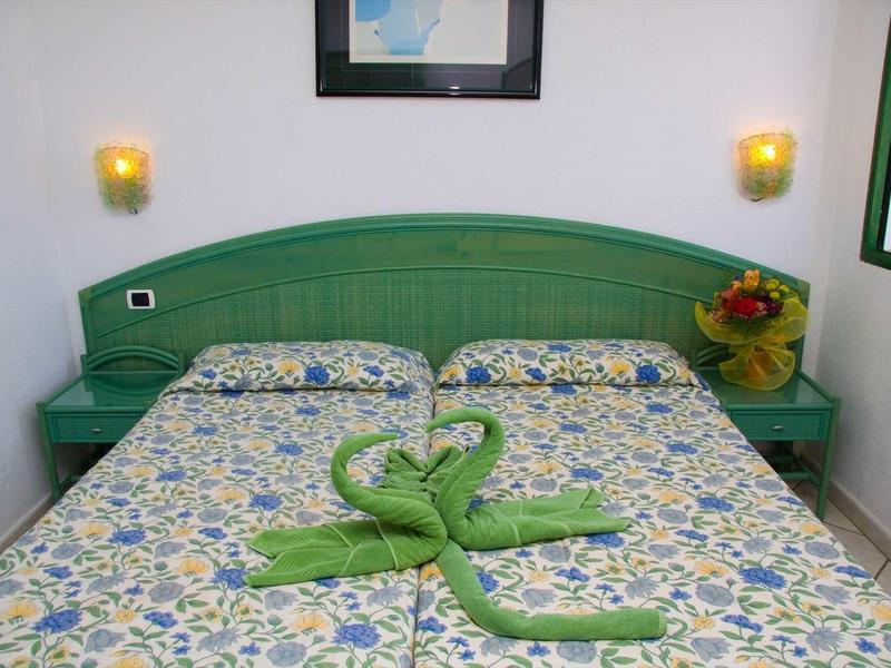 Chambre d'hôtel avec lit double, tête de lit verte et serviettes vertes pliées en forme de cygnes.