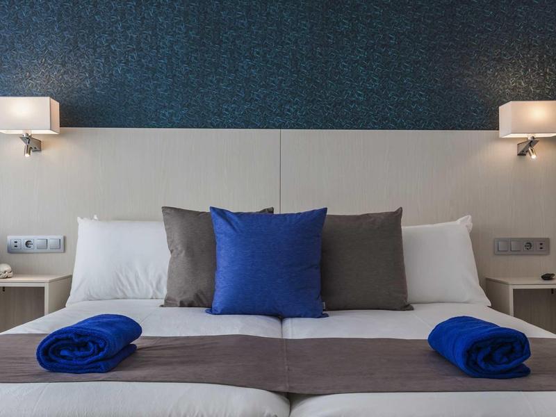 Chambre d'hôtel moderne avec lit double, coussins bleus et éclairage cosy.