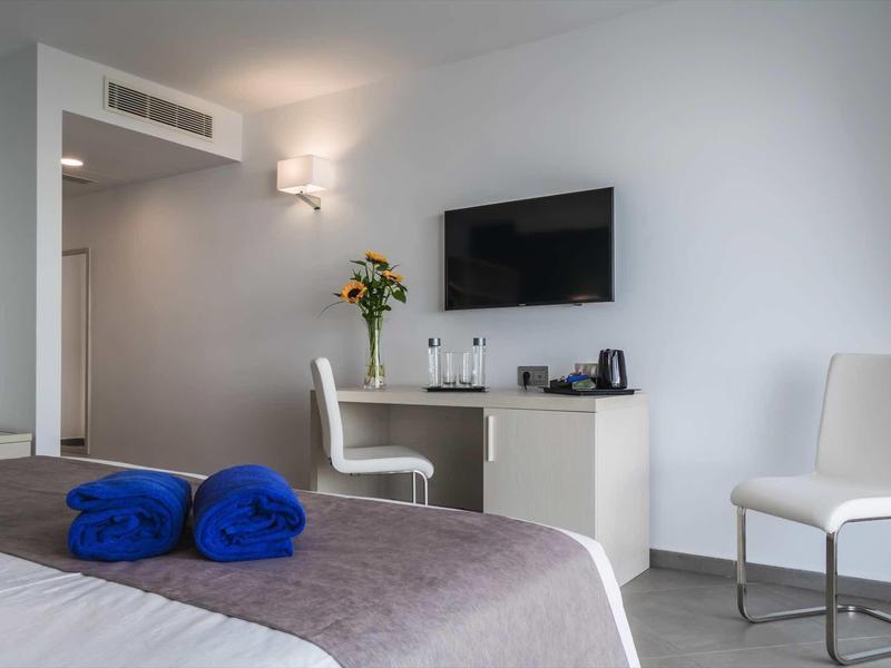 Chambre d'hôtel moderne avec TV, bureau, chaises et deux serviettes bleues sur le lit.