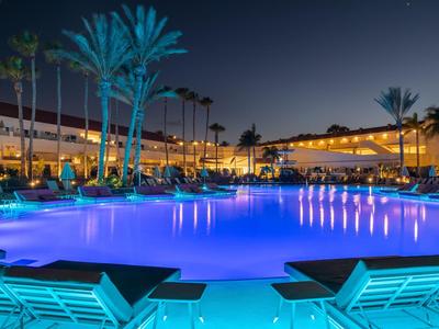 Piscine d'hôtel de nuit avec eau illuminée en bleu et chaises longues autour.