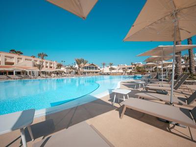Grand piscine d'hôtel avec transats et parasols sous un ciel bleu clair.