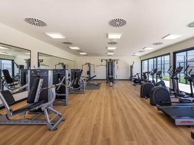 Salle de sport lumineuse avec appareils d'exercice et grandes fenêtres donnant sur la ville.