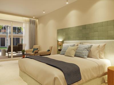 Spacious hotel room with large bed, modern green headboard, chairs, and balcony view.