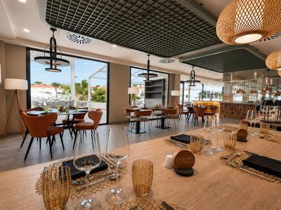 Modern eingerichtetes Restaurant mit Holztischen, Stühlen und großen Fenstern mit Blick nach draußen.