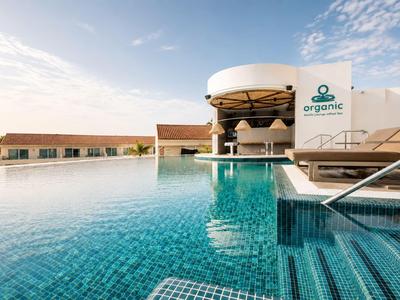 Hotelpool mit klarem Wasser, Liegestühlen und Gebäuden unter blauem Himmel.