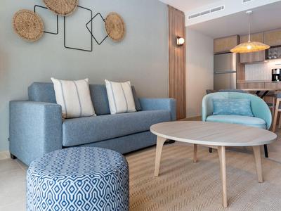 Modern eingerichtetes Wohnzimmer mit blauem Sofa, runden Holztisch und offener Küche im Hintergrund.
