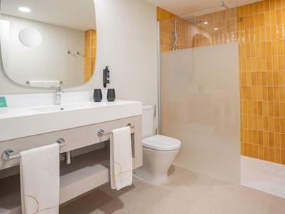 Modernes Hotelbad mit weißem Waschbecken, Toilette und Duschbereich mit gelben Fliesen.