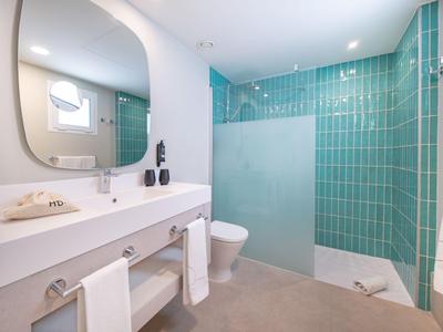 Modernes Hotelbad mit weißem Waschbecken, Toilette und türkisfarbenen Fliesen in der Dusche.
