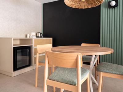 Moderner Essbereich mit rundem Holztisch und vier Stühlen vor dunkelgrüner Wand im Hotelzimmer.
