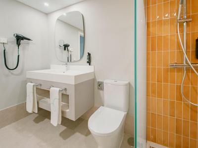 Modernes Hotelbadezimmer mit weißem Waschbecken, Toilette und orangefarbenem Duschbereich.