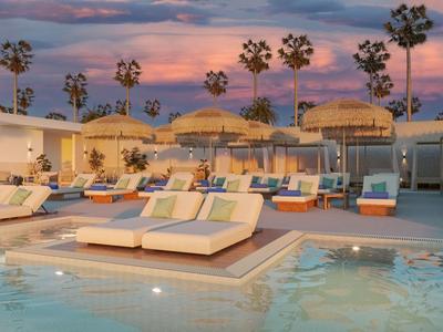 Luxury hotel pool area with sunbeds and palm trees at sunset.