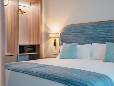 Modernes Hotelzimmer mit Doppelbett, blauen Kissen und warmer Beleuchtung.