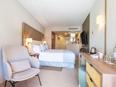 Modernes Hotelzimmer mit Doppelbett, Stuhl, TV und Holzmöbeln in neutralen Farbtönen.