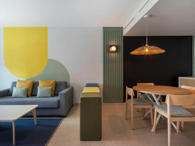 Modern eingerichteter Wohn- und Essbereich mit grauem Sofa, Holzmöbeln und geometrischer Wandgestaltung.