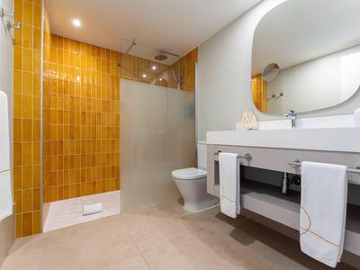Modernes Badezimmer mit gelben Fliesen, ebenerdiger Dusche und großem Spiegel.