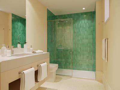 Modern bathroom with green tiled shower, beige walls, sink, and white towels.