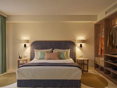 Modern hotel room with a large bed, bedside tables, soft lighting, and an open wardrobe.