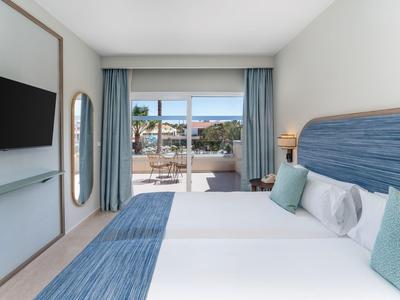 Modernes Hotelzimmer mit Doppelbett, blauen Akzenten und Blick auf Terrasse.