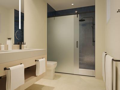 Modern bathroom with beige tiles, floating vanity, glass shower door, and white towels.