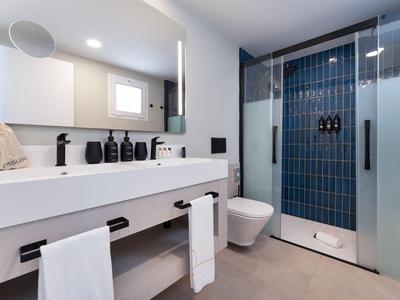 Salle de bain moderne avec double lavabo blanc, douche carrelée bleue et zone toilettes.