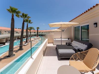 Balcon moderne avec espace salon à côté d'une piscine dans un complexe hôtelier sous un ciel clair.