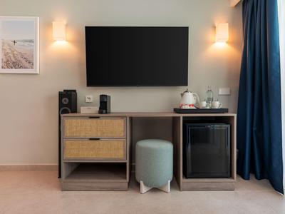 Coin chambre d'hôtel moderne avec téléviseur à écran plat et minibar à côté d'une fenêtre avec rideaux bleus.