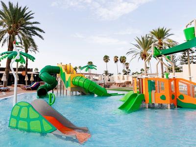 Colorful water playground with slides and palm trees in a sunny pool area.