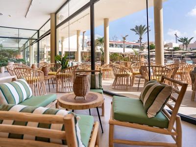 Salon terrasse d'hôtel lumineux avec mobilier en bois donnant sur une piscine et des palmiers.